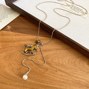 Gros plan du pendentif cheval à bascule doré avec perle sur une chaîne en argent