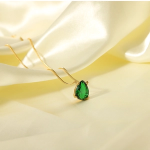 Close-up of 18k gold plated water drop necklace with green zircon on silk background