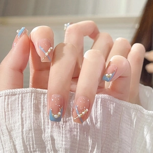 Close-up of nude French press-on nails with blue tips, gold chains and small pearls