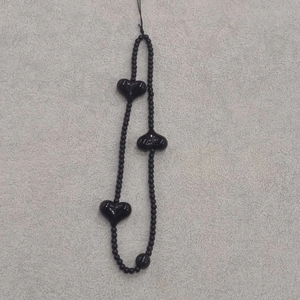 Detail of a black beaded phone strap featuring three 3D heart-shaped charms
