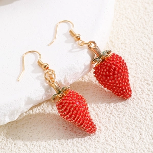 Detalle de pendientes de fresa roja con semillas doradas y hojas verdes sobre piedra