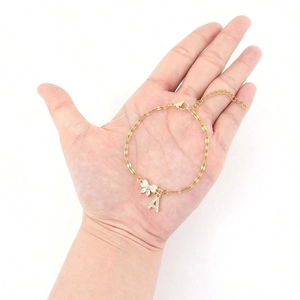 Detail view of a gold chain bracelet featuring a bow charm and a sparkling letter A charm
