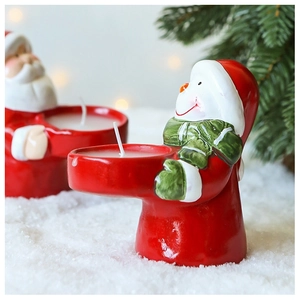 Close-up of Santa Claus and snowman ceramic candle holders on artificial snow background