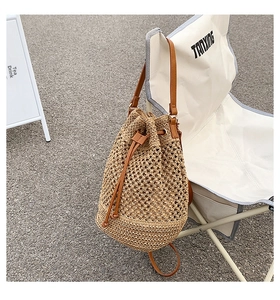 Detail of hollow-out woven paper straw bucket bag with leather strap in outdoor setting
