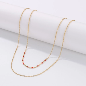 Détail d'un collier doré à double rangée avec petites perles en émail rouge sur présentoir