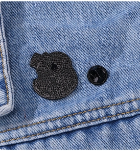 Close-up of cute snake gentleman enamel pin with black rubber clutch on denim fabric