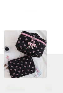 Detailed scene of black quilted makeup bag set featuring pink bow patterns and pearl charms