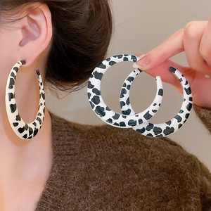 Detail of wide flat hoop earrings featuring classic black and white cow print glossy finish