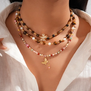 Macro detail of triple-layer necklace featuring tiger eye stones, pearls and bow pendant