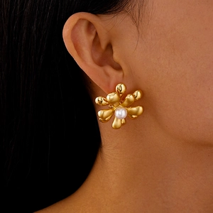 Détail d'une boucle d'oreille fleur dorée avec une perle centrale sur un lobe