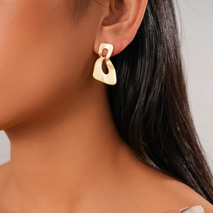 Close-up of gold irregular geometric interlocking drop earrings worn by a model