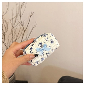 Detail of white corduroy mini pouch with blue floral patterns and a small blue bow