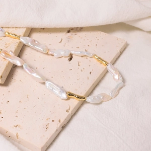 Baroque pearl necklace with gold textured beads on a minimalist stone background