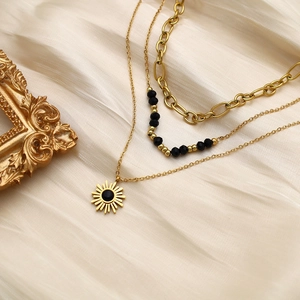 Detailed close-up of triple-layered gold sun pendant necklace with black beads on silk