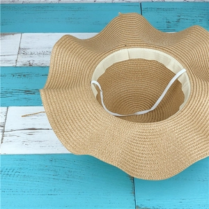Détail d'un chapeau de paille à bord ondulé avec bandeau intérieur sur fond en bois