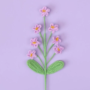 Macro shot of 7-head purple hand-knitted crochet flowers with green leaves on purple base