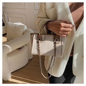 Detail of beige canvas bucket bag with brown leather handles and decorative metal chain