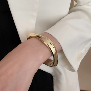 Detail of wavy golden irregular bangle on model with polished mirror finish surface