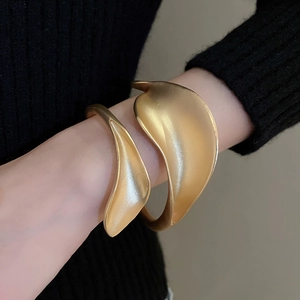 Close-up of matte gold open cuff bracelet with leaf design worn on a black knit sleeve