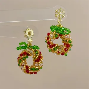 Detail of handmade beaded Christmas wreath earrings with gold snowflake stud and red accents