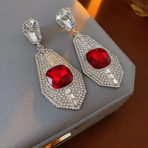 Macro detail of silver needle earrings with red square crystal and diamond inlay