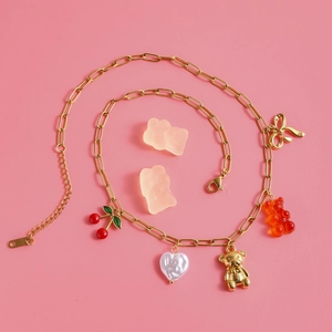 Detailed view of gold necklace featuring cherry, teddy bear, and heart charms on pink