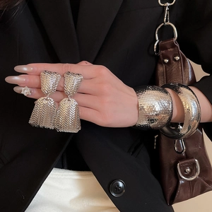 Detailed close-up of textured silver geometric earrings and wide hammered metal cuff bracelet