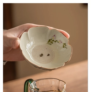 Detail of hand-painted daisy ceramic tea strainer filtering tea into a glass pitcher