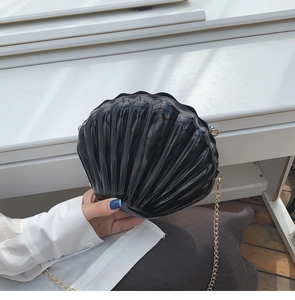 Close-up of black shell-shaped evening bag with glossy texture and gold chain strap