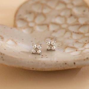 Classic silver stud earrings with four cream pearls in a flower shape on ceramic dish