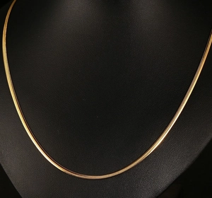Close-up of golden stainless steel flat snake chain necklace on a black mannequin bust