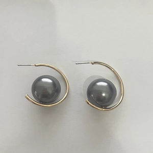 Detailed close-up of C-shaped gold earrings featuring large dark grey lustrous pearls