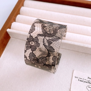 Detail of wide acrylic cuff bracelet featuring black lace floral patterns in jewelry box