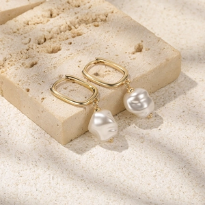 Detail of gold square hoop earrings with irregular baroque pearls on natural stone