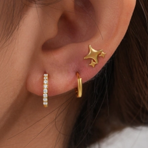 Close-up of golden earring set featuring crystal hoop, plain ring and star stud on ear