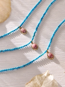 Detail of blue beaded long necklace with pink stone pendant in twisted gold frame