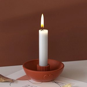 Terracotta ceramic candle holder with heart relief and white pillar candle in warm ambient light