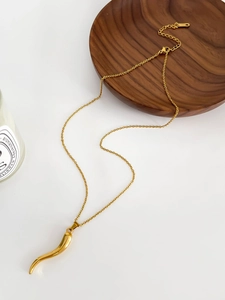 Detailed macro view of the gold Italian horn pendant necklace on a minimalist wood tray