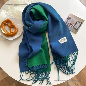 Detail of blue and green cashmere-feel scarf with tassels on white minimalist table