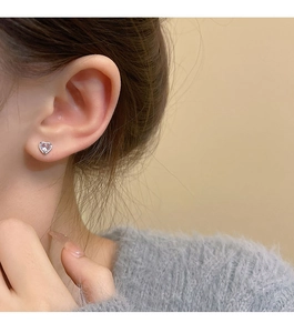 Close-up of a silver heart stud earring with pink zircon on a model's ear