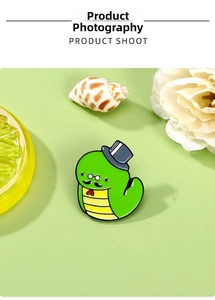 Close-up of green cartoon snake enamel pin with top hat and bow tie on pastel background