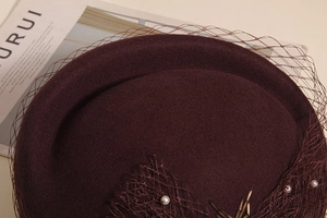 Close-up of burgundy wool beret featuring elegant mesh veil and pearl bead details