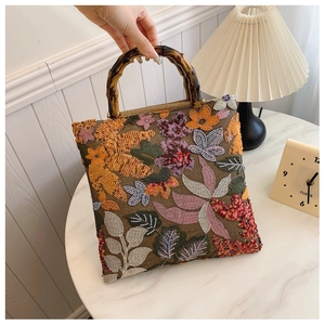 Detailed view of sequined floral embroidery on a linen handbag with bamboo handle