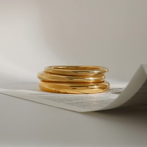Close-up of three stacked 18k gold-plated stainless steel bangles with polished mirror finish