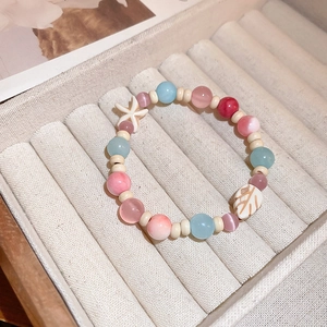 Macro detail of beaded bracelet featuring opal-like beads with starfish and leaf charms