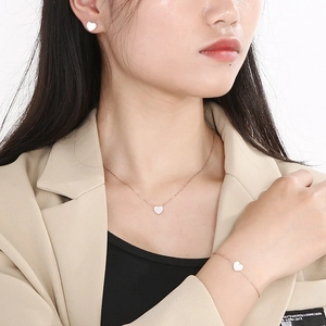 Detail of rose gold jewelry set with white heart pendants worn by a model