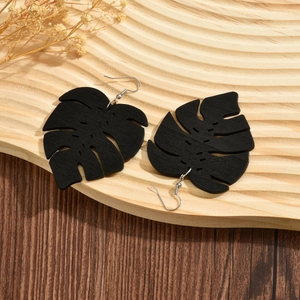 Chic black wooden monstera leaf earrings with silver hooks on a natural rustic tray