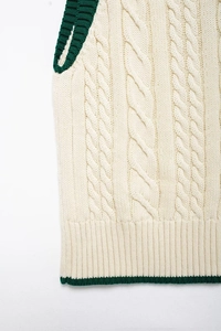 Close-up of cream cable knit vest showing green contrast trim and ribbed texture details
