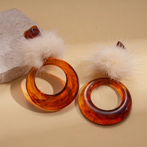 Retro amber resin hoop earrings with white fluffy pom-poms on a textured stone