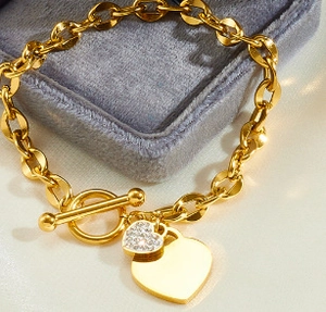 Detail of gold heart pendant bracelet with T-bar toggle clasp on gray velvet display